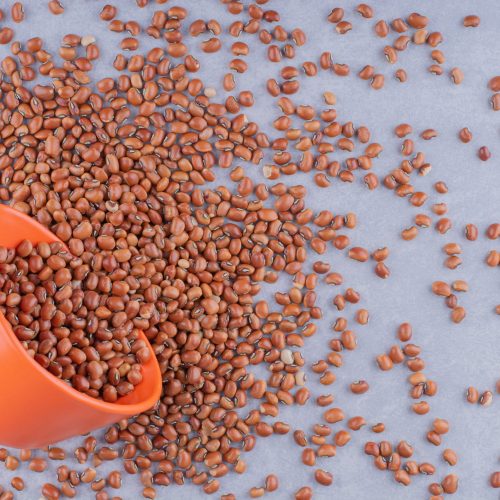 Small orange bowl lodged in a pile of red beans on marble background. High quality photo