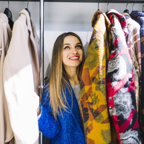 smiling-young-woman-looking-coats-hanging-rack